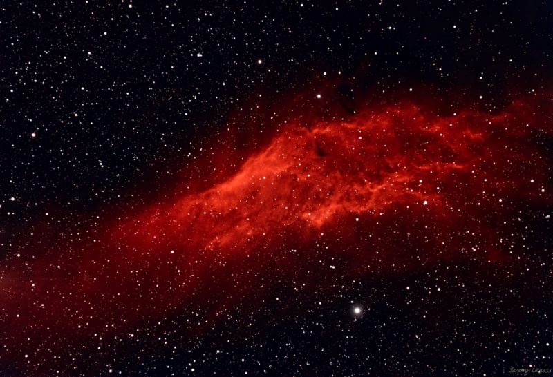 Large, bright red cloud of gas in deep sky over a multitude of distant stars.