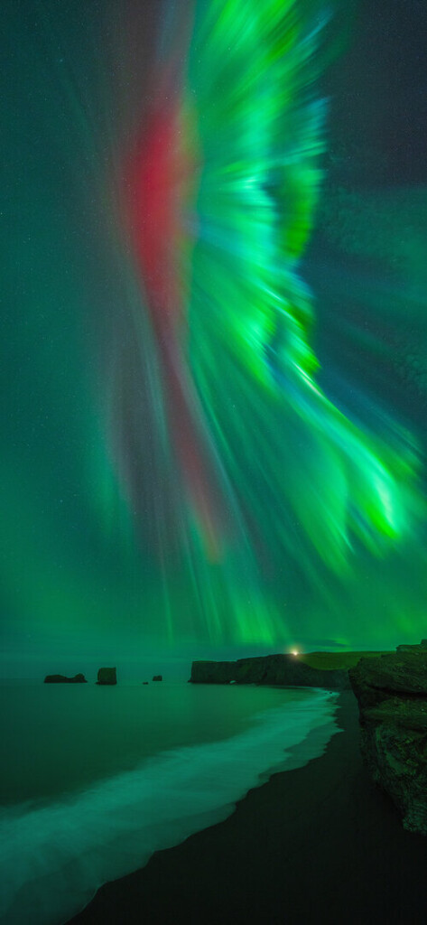 Tall, thin red streak in the sky with glowing green fans of light, like bird wings, to one side.