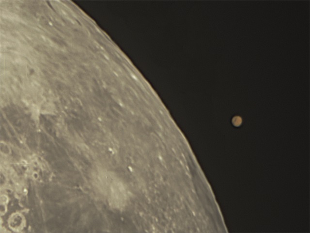 Side of moon with tiny orange Mars large enough to see a dark marking on it.