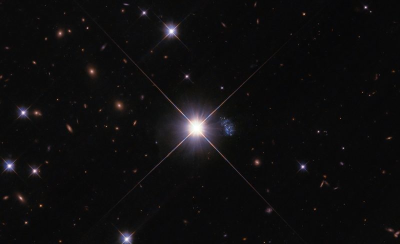 A bright star at center with a bluish fuzzy patch, the Peekaboo Galaxy, to the right.