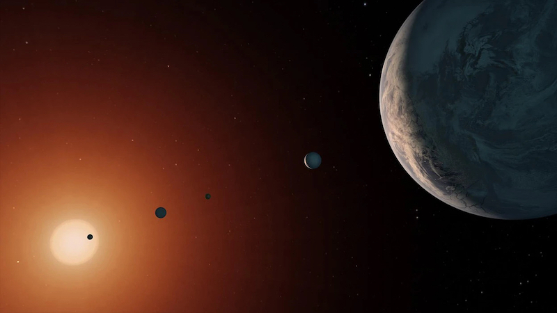 TRAPPIST-1: Large mottled planet in foreground with smaller planets in line toward small star.
