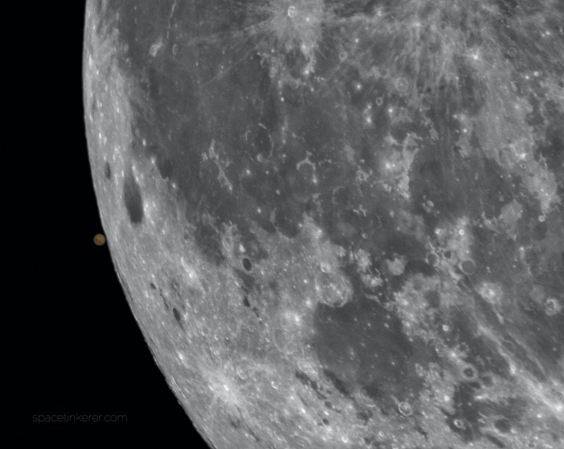 Section of gray moon with tiny, slightly marked Mars touching it.