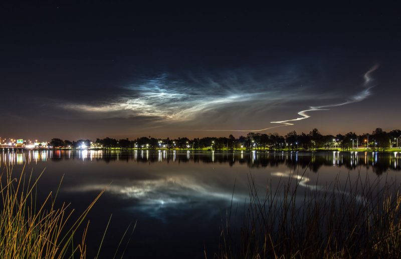 Eerie white and blue thin clouds shining in a dark sky and reflected over a pond.
