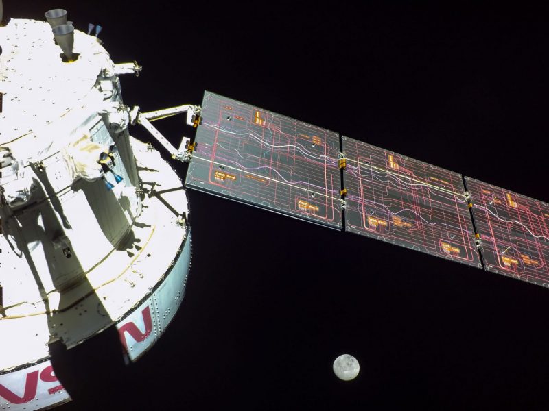 Artemis 1: Sunlit side of spacecraft with solar panel, and small gray moon in distance.