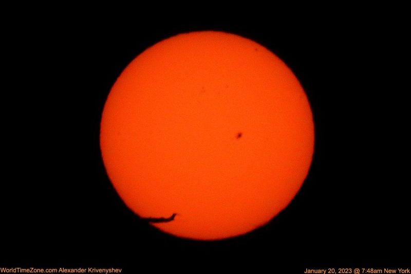 The sun, seen as a large orange disc with an airplane flying accross.