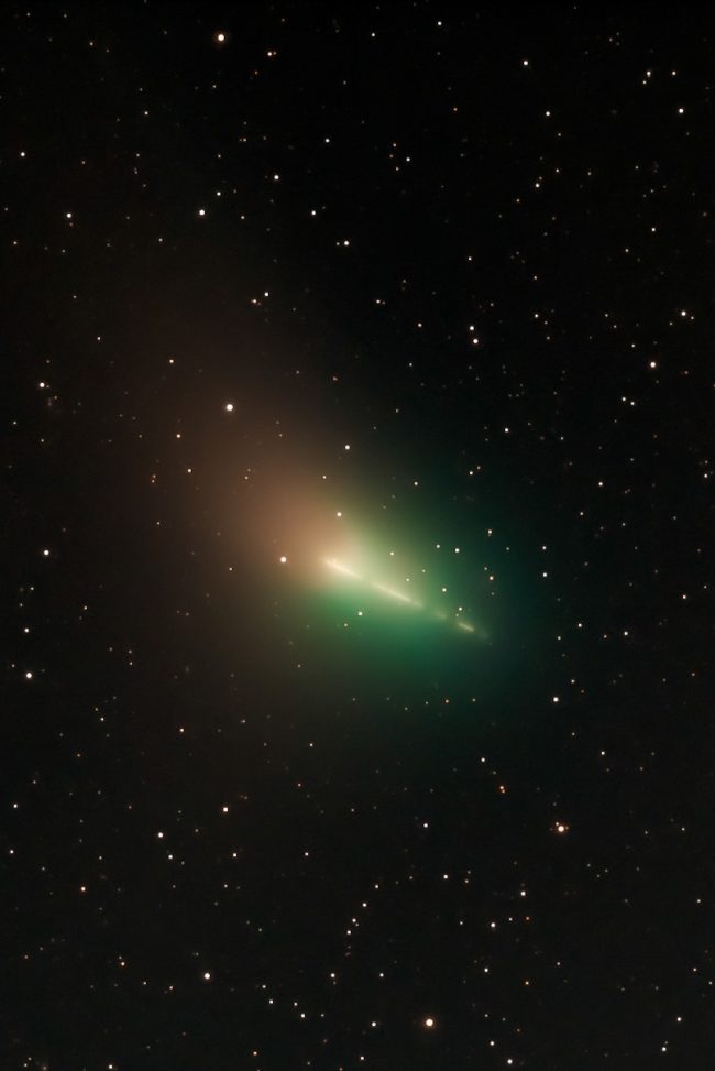 Comet with streaks of green in time lapse and fuzzy halo around it.