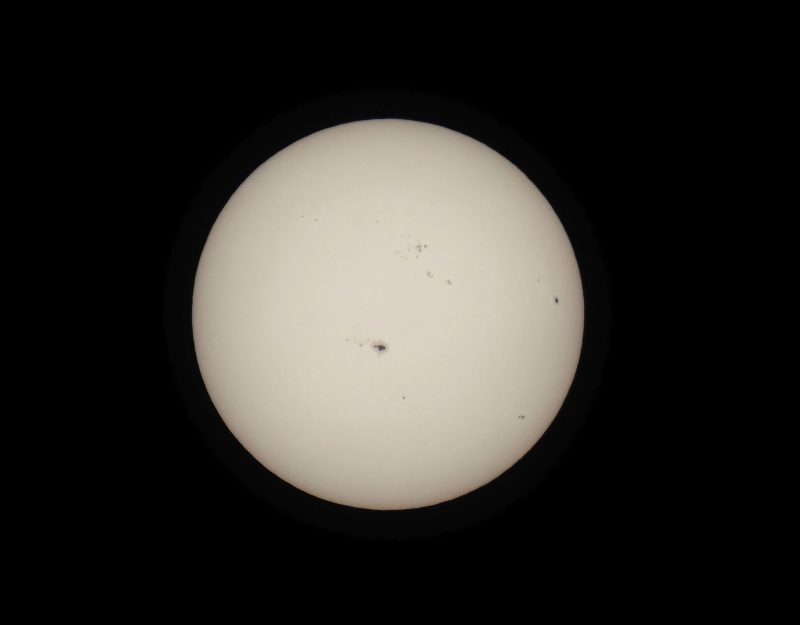 The sun, seen as a large whitish sphere with small dark spots.