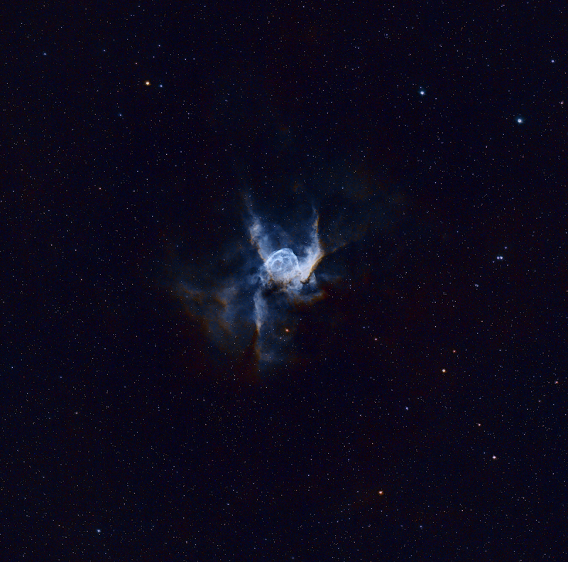 H-shaped, bright blue cloud of gas in the deep sky, over a multitude of distant stars.