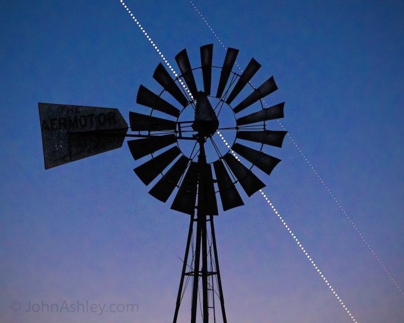 Photos of Venus-Saturn conjunction: Two straight lines of bright dots, one brighter, diagonal in a blue sky behind an old-fashioned windmill.