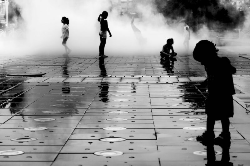Black-and-white photo showing silhouettes of children playing in fountain.