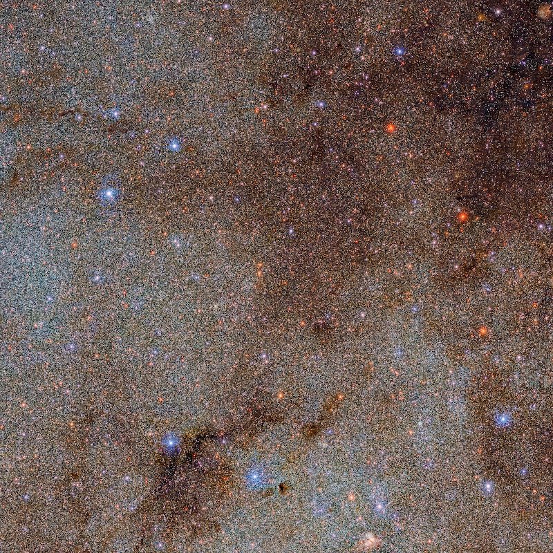 Extremely dense field of millions of tiny stars punctuated by a few brighter red and blue stars.