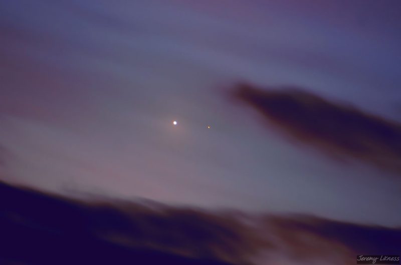 Much-brighter Venus on the left, and fainter Saturn on the right, between ragged purple clouds.
