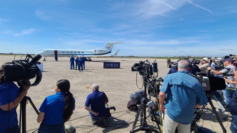 Photographers in foreground, 4 astronauts in background, on a tarmac.