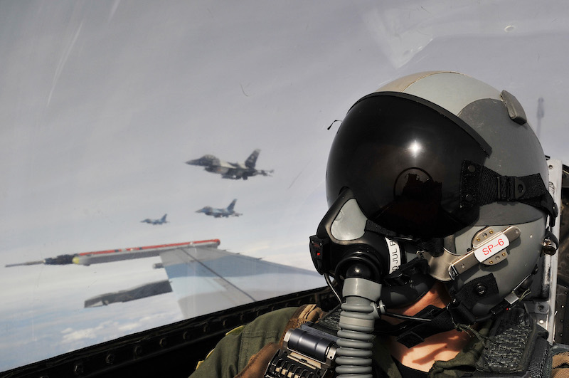 Brain changes in fighter pilots: Pilot with helmet in a fighter jet cockpit, with 3 other jets in midair near him.