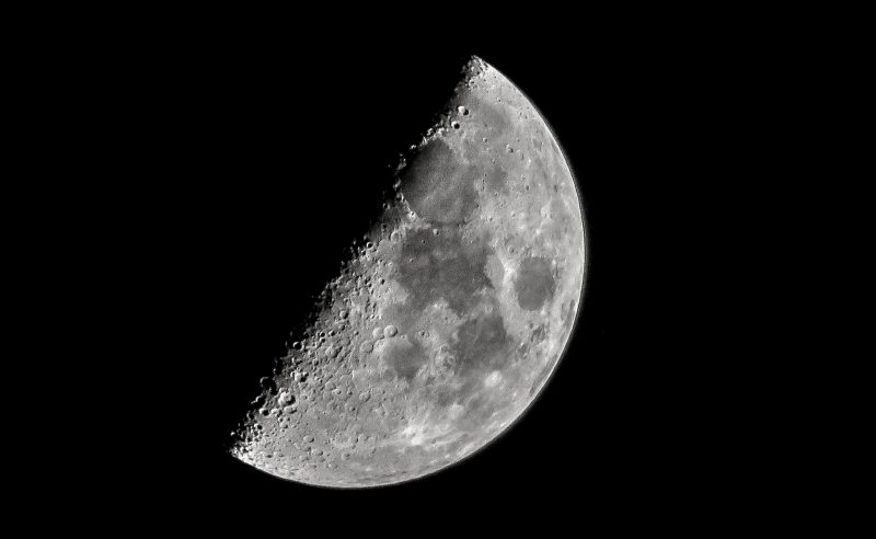 Half illuminated moon at 1st quarter. At its illuminated side, there darker areas and many craters.