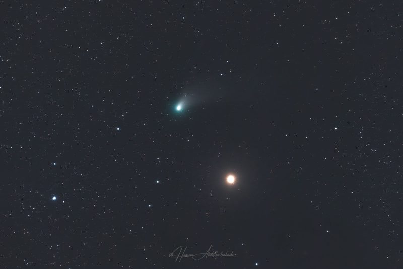 A bright, green comet over a background of distant stars.