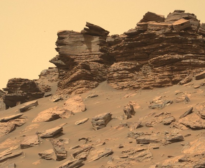 Life on Mars: Finely layered rock outcrops in reddish sandy landscape.