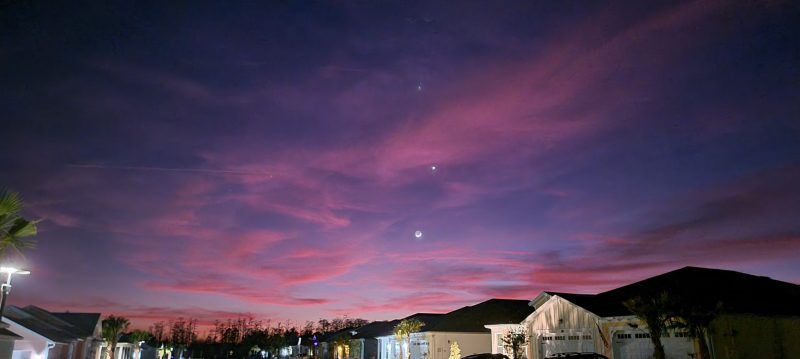 Pink sunset with crescent moon at bottom and 2 bright dots spaced out above, through pink clouds.