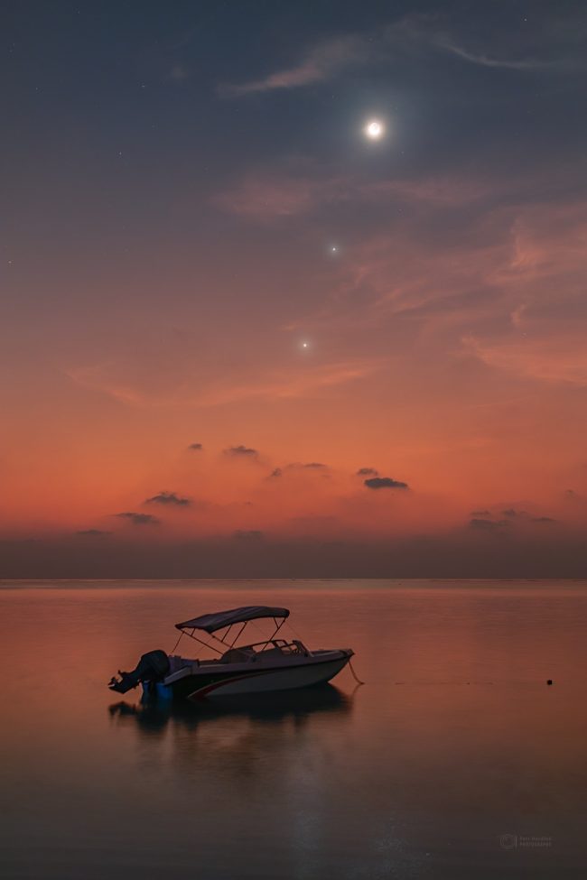 Boat resting in water at sunset with 2  lights above and moon at top.