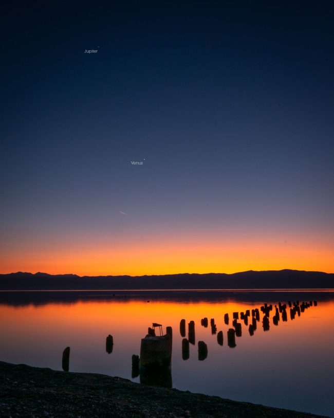 Sunset colors over lake and pier stumps with 2 labeled dots marking Venus and Jupiter in the sky.