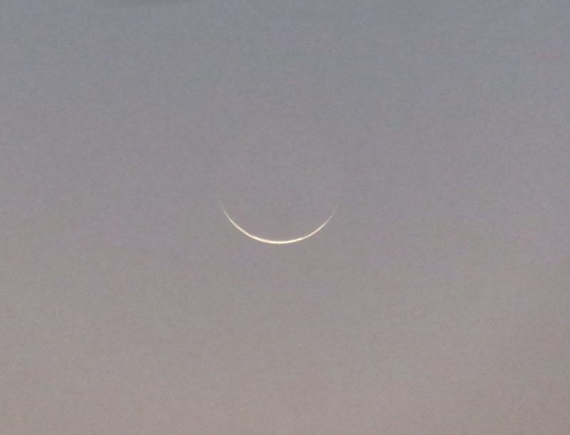 A sliver of a waning crescent moon against a grayish sky.