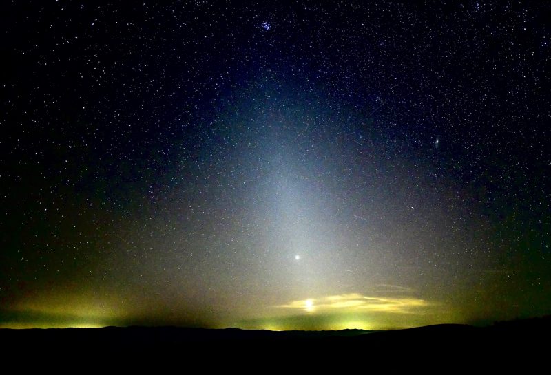 Nightsky with dark horizon in the foreground. Fuzzy cone of light and 2 bright planets.