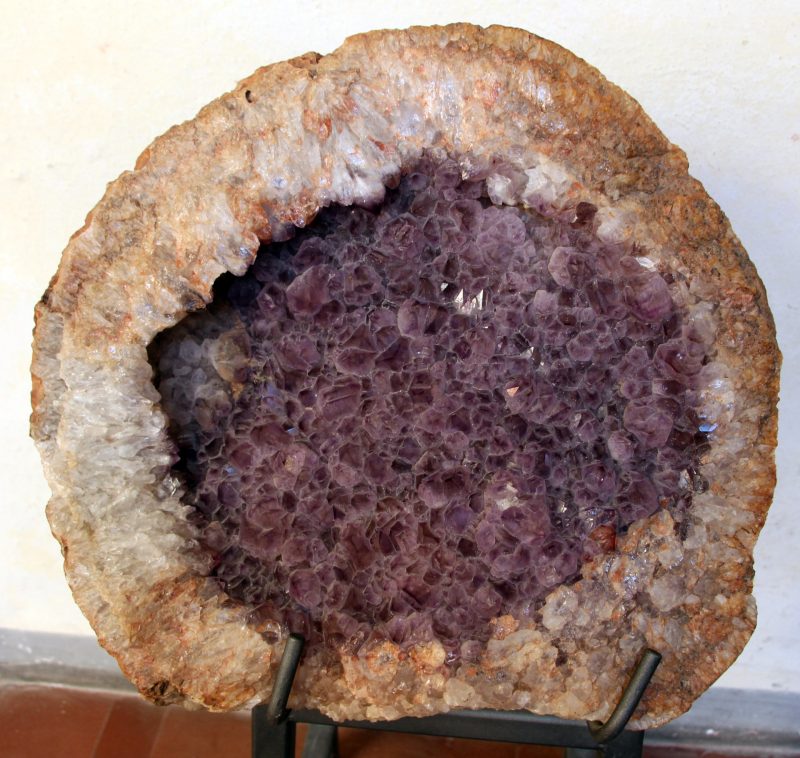 Broken-open rock with thick brown outer layer and purple crystals within.