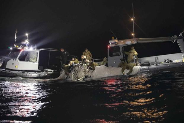 People in military clothing on a boat, at night, with lights shining into the water.