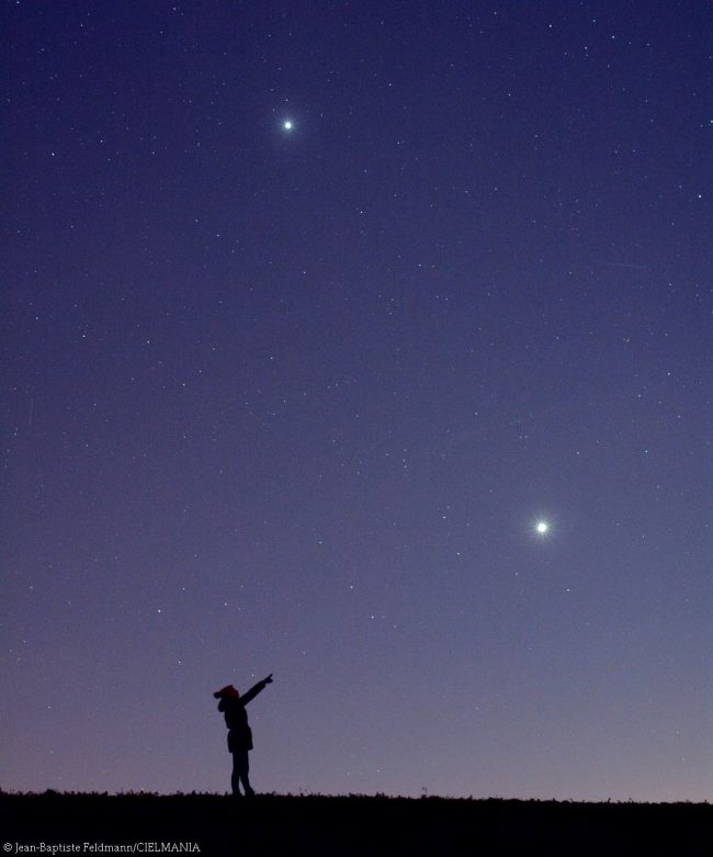 Silhouette of a girl pointing toward bright planets Venus and Jupiter in deep purple sky.