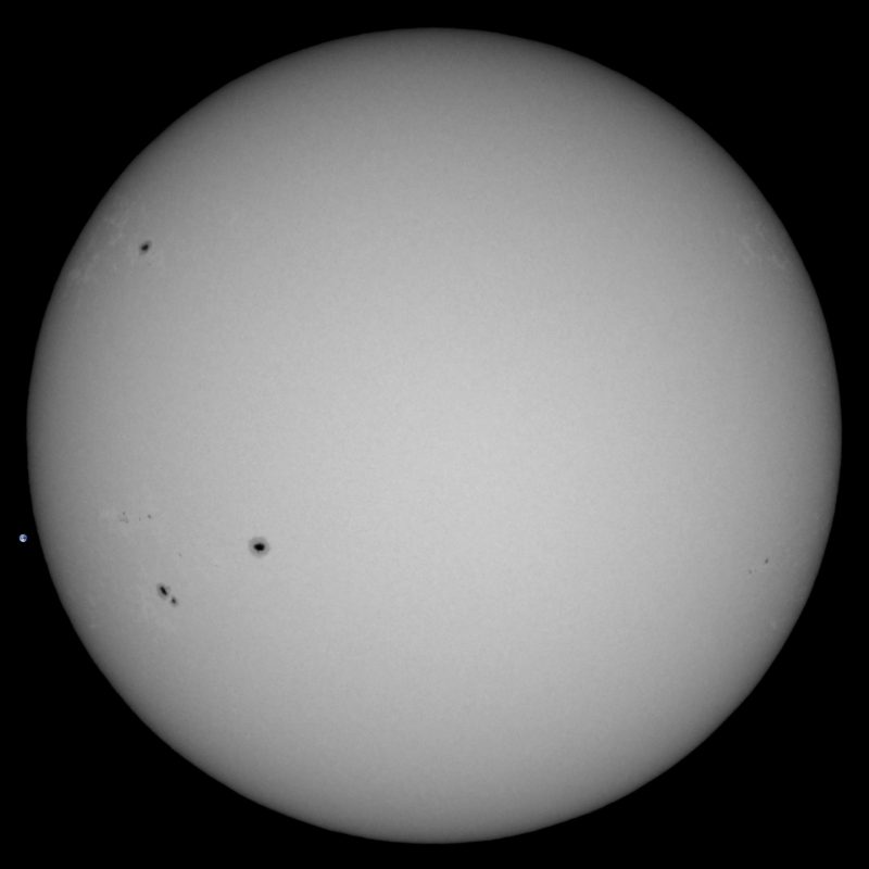 The sun, seen as a large white sphere with small dark spots.