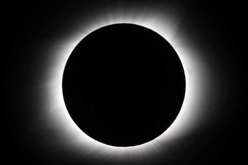 Total eclipse of the sun with bright corona around solid black circle.