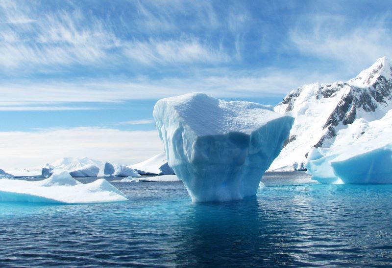 Antarctic meltwater: A top-heavy iceberg surrounded by blue water with snowy land behind.