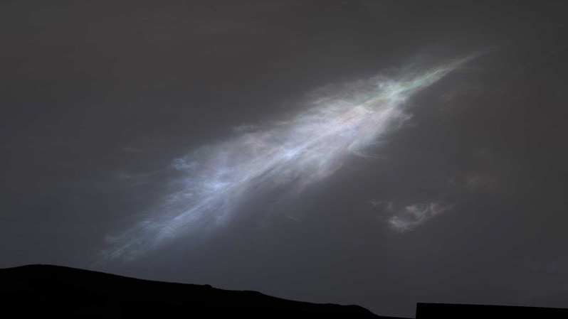 Feather-shaped cloud against dark gray sky, mostly white, but it shows other pale colors.