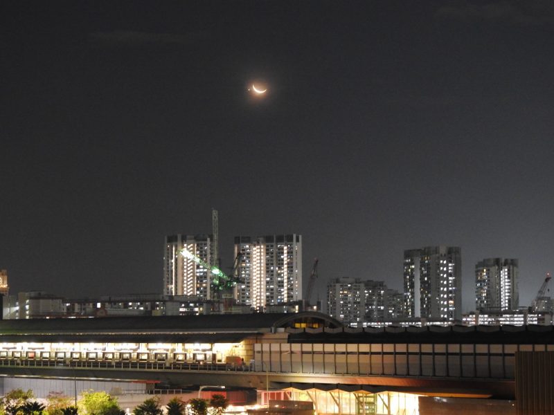 Cityscape below with glowing crescent moon and a dot beside it above.