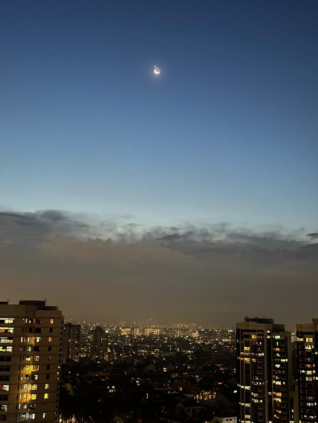 Lights of a city below with clouds and clearing showing moon and dot on top.