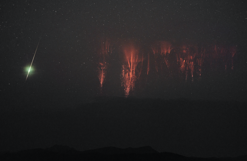 Bright green streak of a meteor, and red jellyfish-like tendrils hanging down in a dark sky.