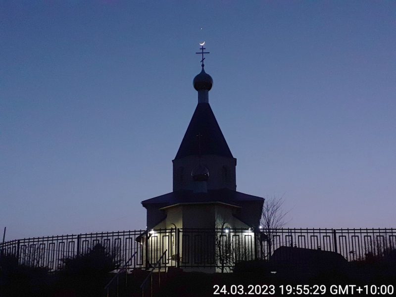 Church steeple with crescent moon positioned on top and bright dot of Venus above that in twilight sky.