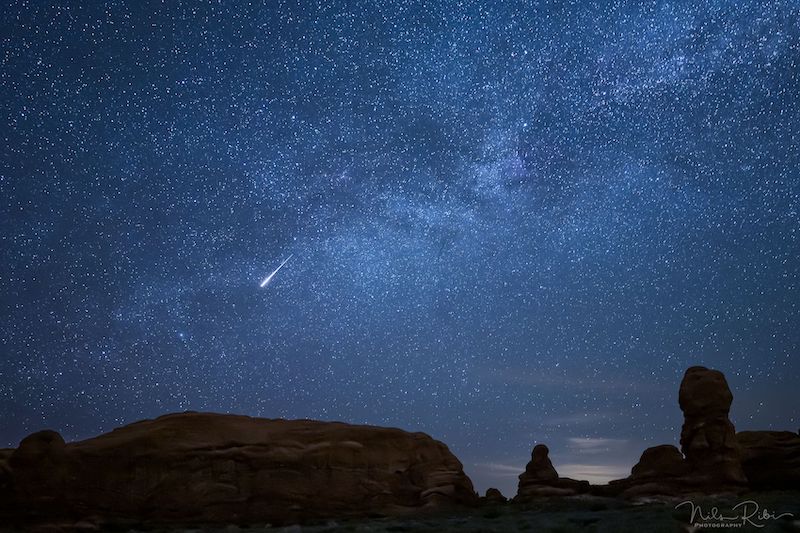 How high up are meteors: Bright streak in densely starry sky crossed by Milky Way, with rock formations in foreground.