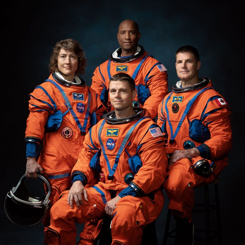 Group of 4 astronauts in orange jumpsuits. One white woman, a black man, and two white men.