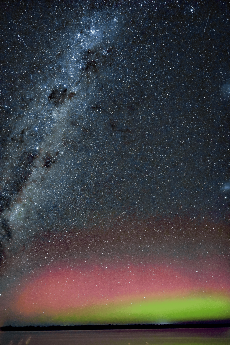 Densely starry night sky with the Milky Way at left and green and pink glow near horizon.