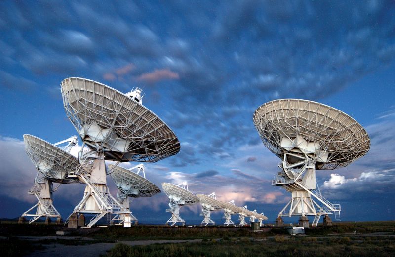 10 white dish-shaped radio telescopes under blue sky with patchy clouds.