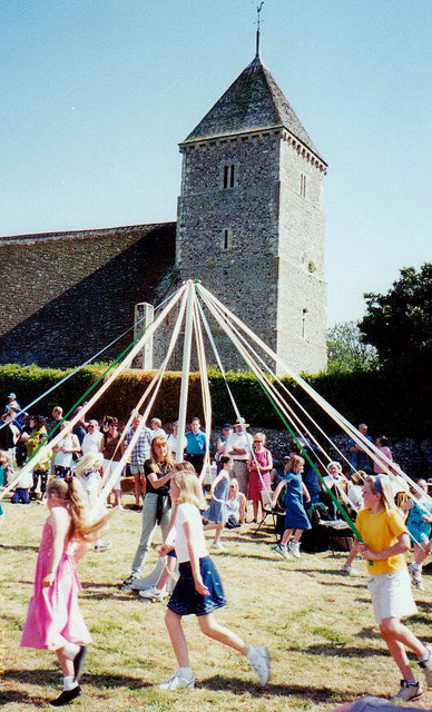 Children holding on to ribbons off a maypole and church in the background.