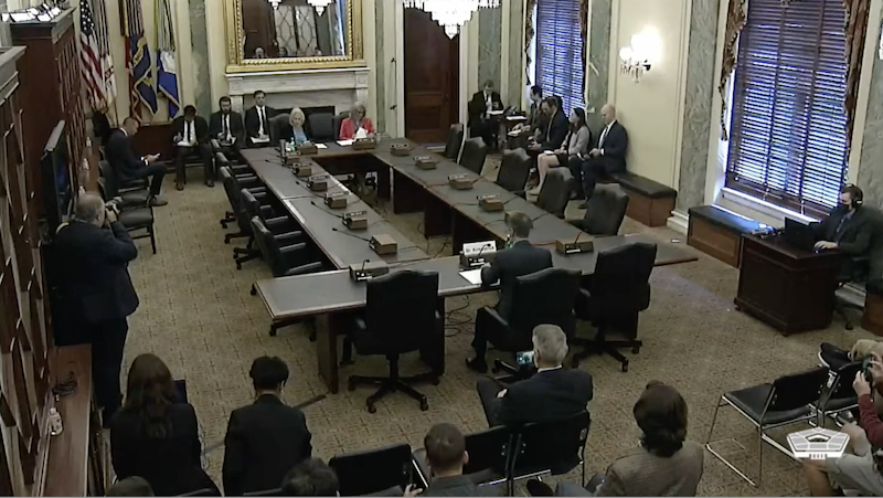 UFO hearing: Group of formally-dressed people standing around in stately-looking room with long tables.