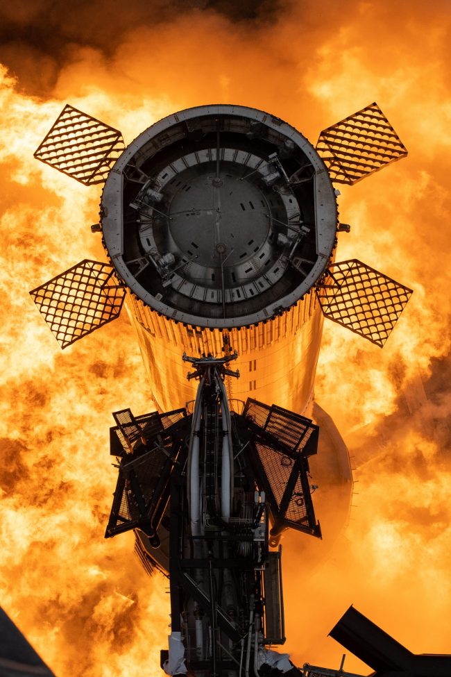 Chrome cylinder viewed from the top standing in a huge mass of orange and yellow flame.