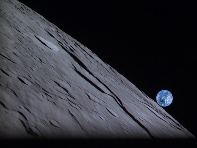 1st private moon lander: An angled view of cratered moon closeup with perfect blue globe of Earth over moon's limb.