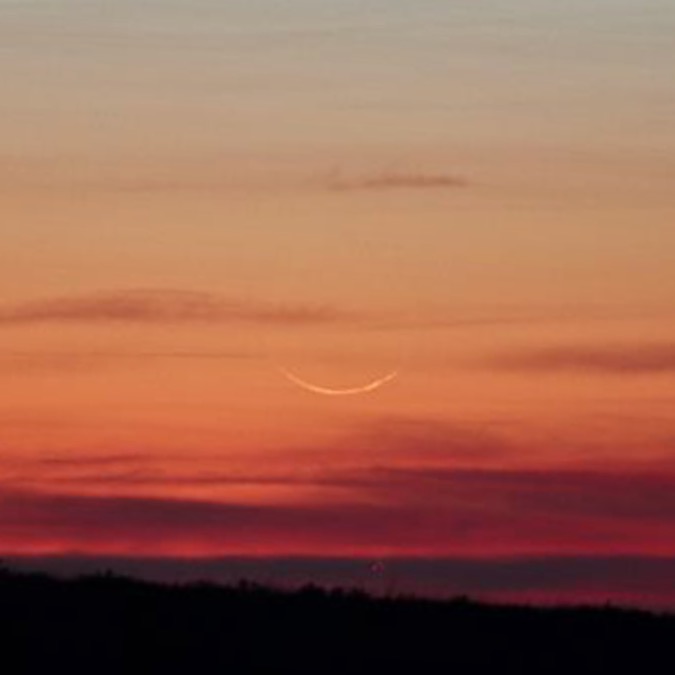 Slim crescent moon, dark horizon, twilight sky.