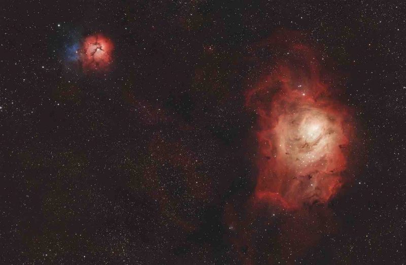 Two clouds of red-colored gas over a multitude of distant stars.