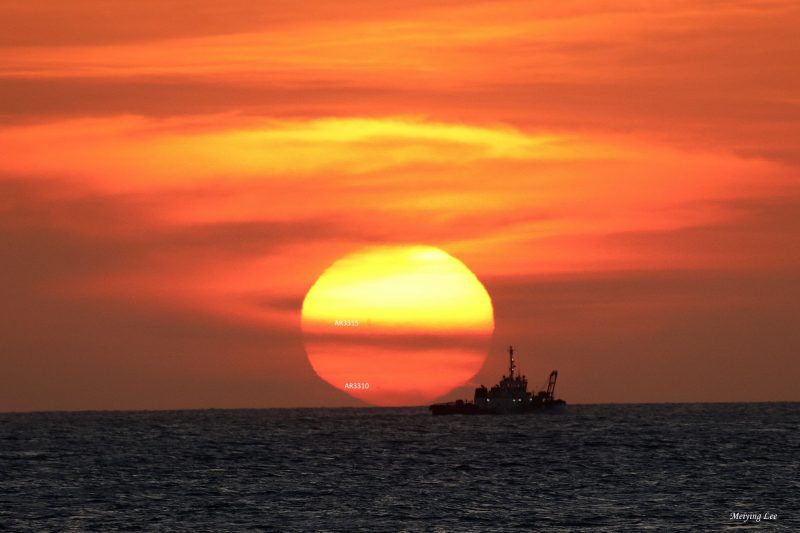 Orange sun setting over the ocean, with the silhouette of a ship at a distance.