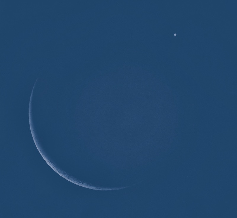 Thin crescent moon and Jupiter in blue sky.