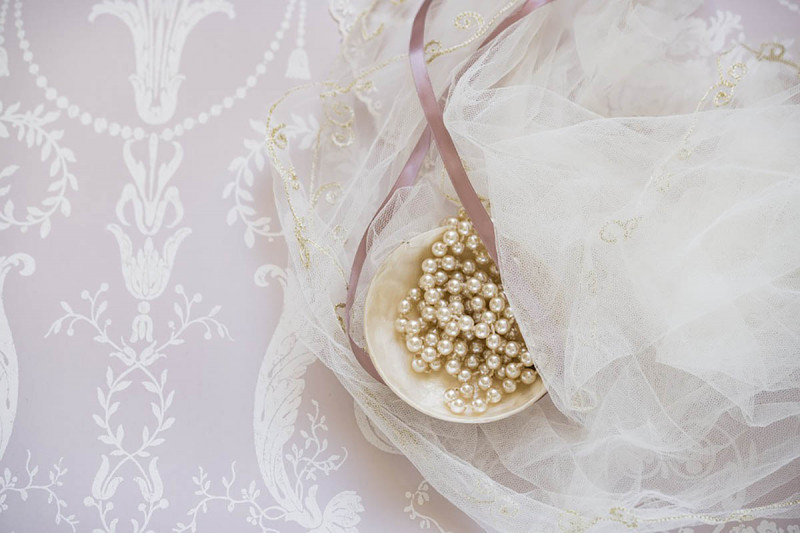 Strand of pearls with a ribbon and transparent lace in the background.